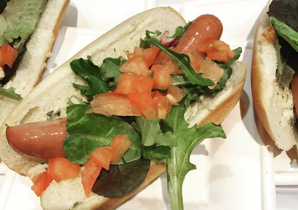 Up close view of bacon hot dog topped with lettuce and tomatoes